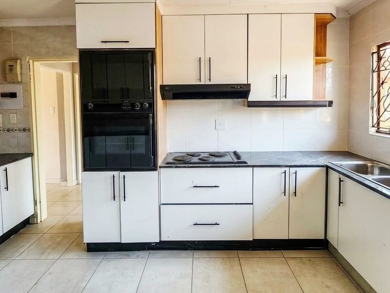 A functional kitchen featuring built-in cabinetry, an integrated oven and hob, double basin sink, and tiled splashbacks, offering a clean and practical workspace.