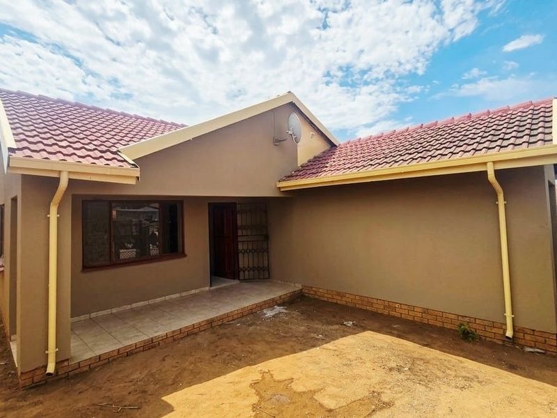 Rear view of a modern house featuring a tiled roof, covered patio area, and unfinished garden space.