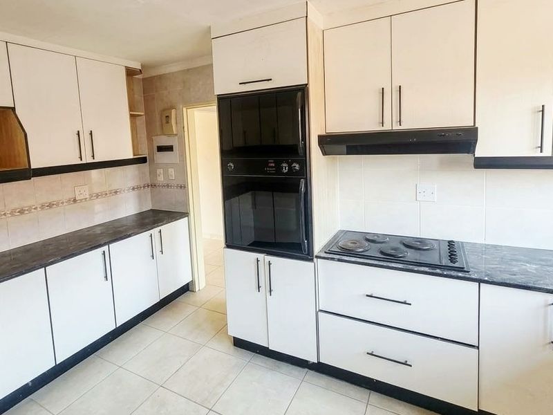 A functional kitchen featuring white cabinetry, dark laminate countertops, built-in oven, electric hob, and tiled flooring, offering a clean canvas for potential updates.