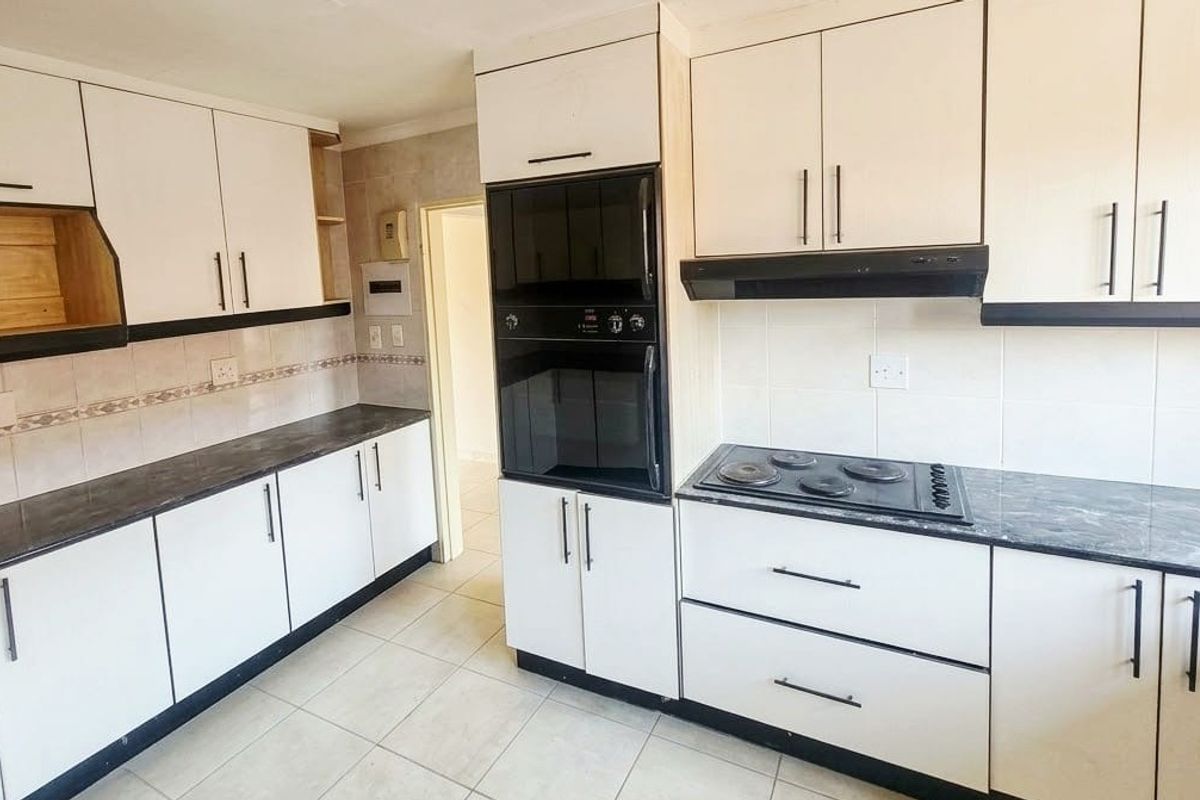 A functional kitchen featuring white cabinetry, dark laminate countertops, built-in oven, electric hob, and tiled flooring, offering a clean canvas for potential updates.