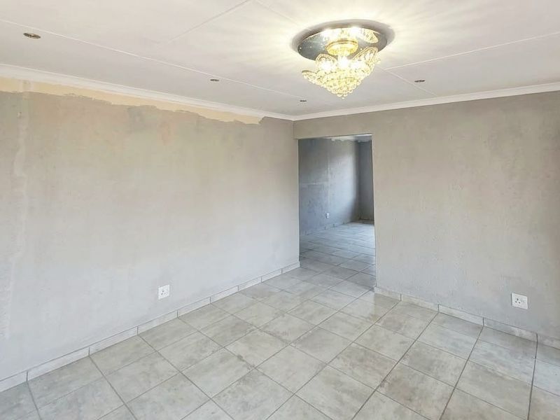 An empty living room featuring tiled flooring and a central light fixture, currently requiring wall finishing and painting to complete the space.