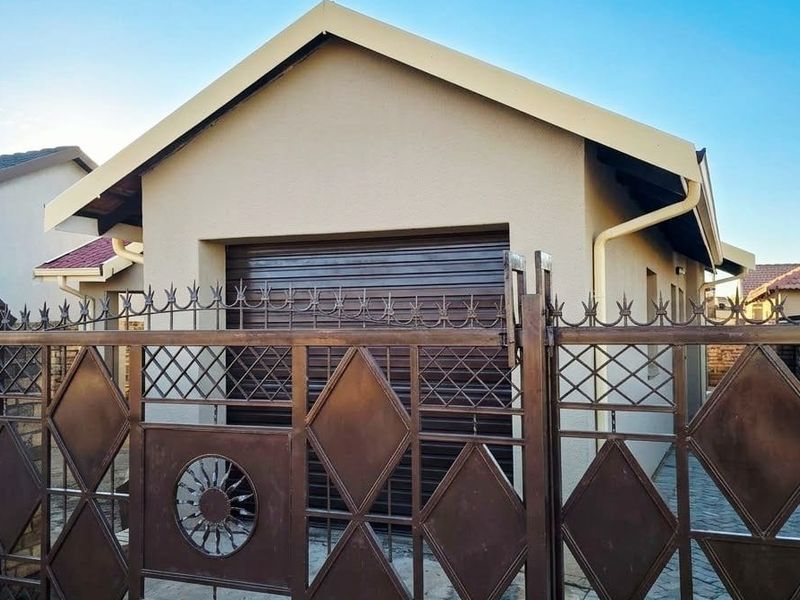 Front view of the property featuring a secure metal gate, roller garage door, and well-maintained plastered exterior walls with tiled roofing.