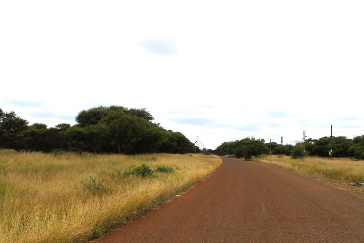 A view of the asphalt road leading towards the vacant residential land, featuring surrounding natural vegetation and overhead power lines.