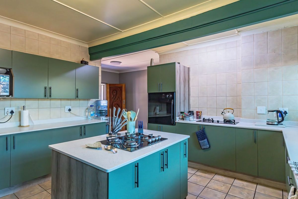 A functional kitchen featuring green cabinetry, a central island with a gas hob, built-in oven, and tiled backsplash.