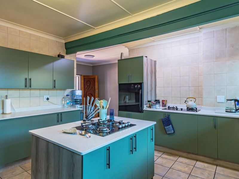 A functional kitchen featuring green cabinetry, a central island with a gas hob, built-in oven, and tiled backsplash.