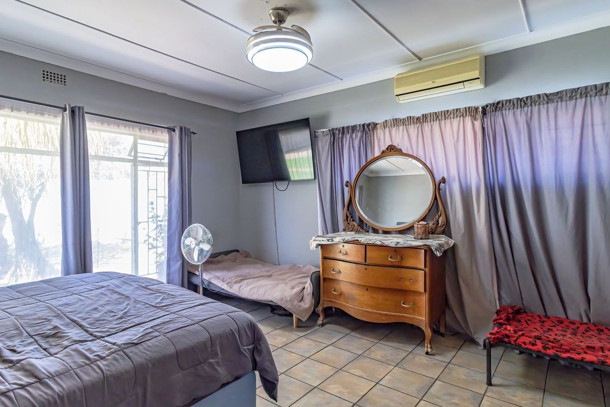 A bedroom featuring tiled flooring, a ceiling fan, and a wall-mounted air conditioning unit, with direct access to the exterior via a sliding glass door.