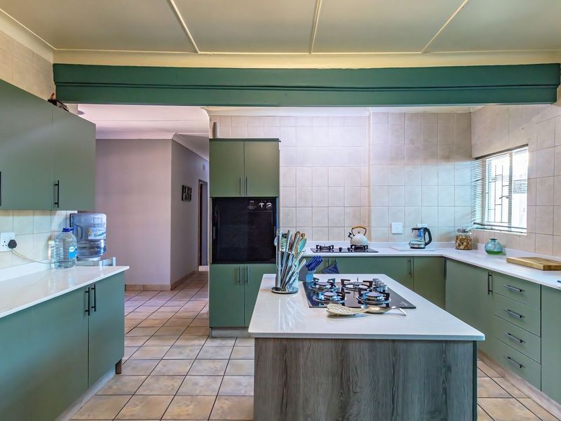 A well-maintained kitchen featuring sage green cabinetry, a central island with a gas hob, stone countertops, and tiled splashbacks.