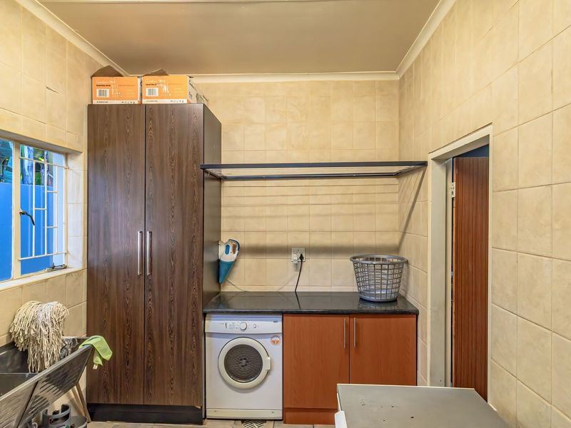 Functional laundry room featuring tiled walls, built-in cabinetry, a stainless steel sink, and a wall-mounted drying rack for efficient utility space.