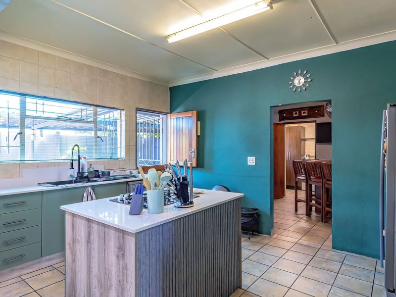 A functional kitchen featuring a central island with a gas hob, tiled flooring, and ample built-in cabinetry, with an adjacent scullery area.