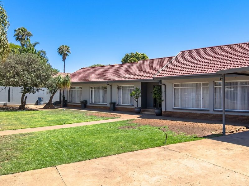 Front view of a single-story house featuring a tiled roof, concrete driveway, carport, and a spacious front garden with perimeter walling.