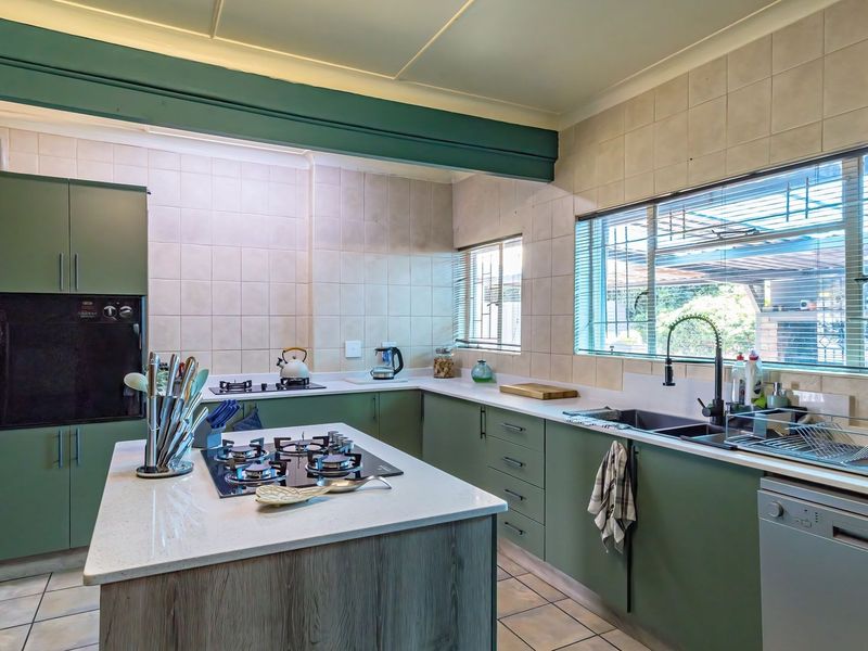 A functional kitchen featuring green cabinetry, stone countertops, a central island with a gas hob, and a double sink with tiled backsplash.