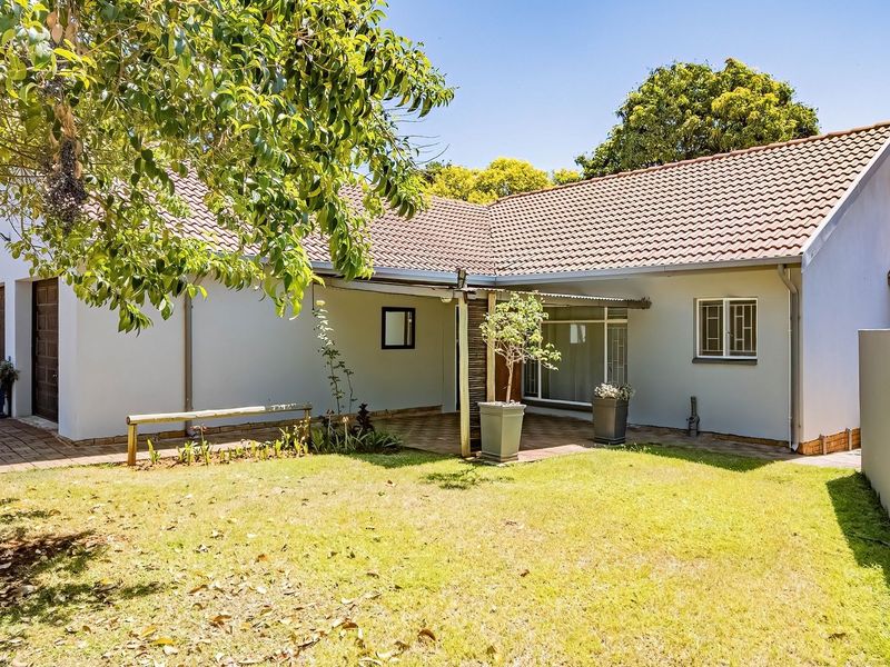 A well-maintained rear exterior view of the house featuring a paved patio area, a neat lawn, and a tiled roof structure.