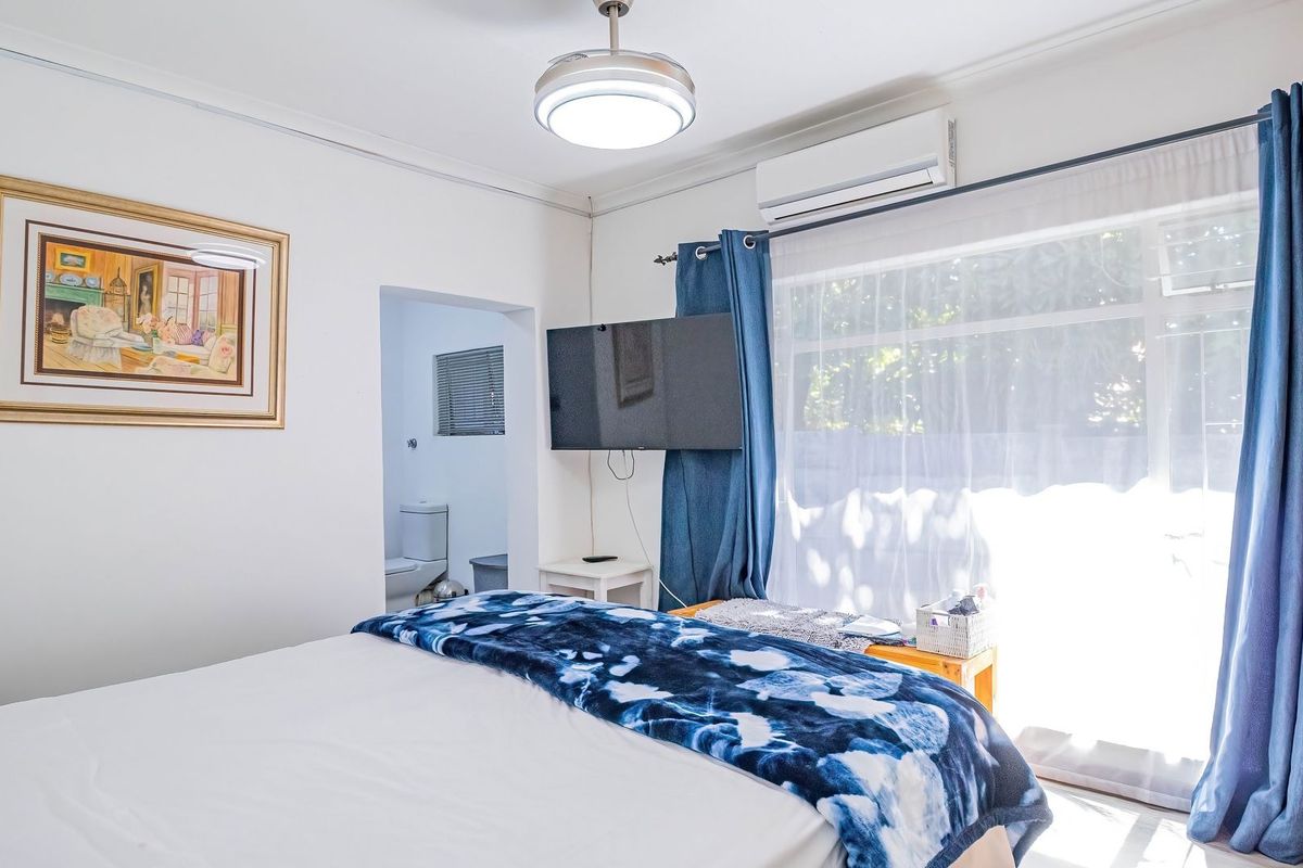 A well-lit bedroom featuring an en-suite bathroom, air conditioning unit, and large sliding glass doors providing natural light.