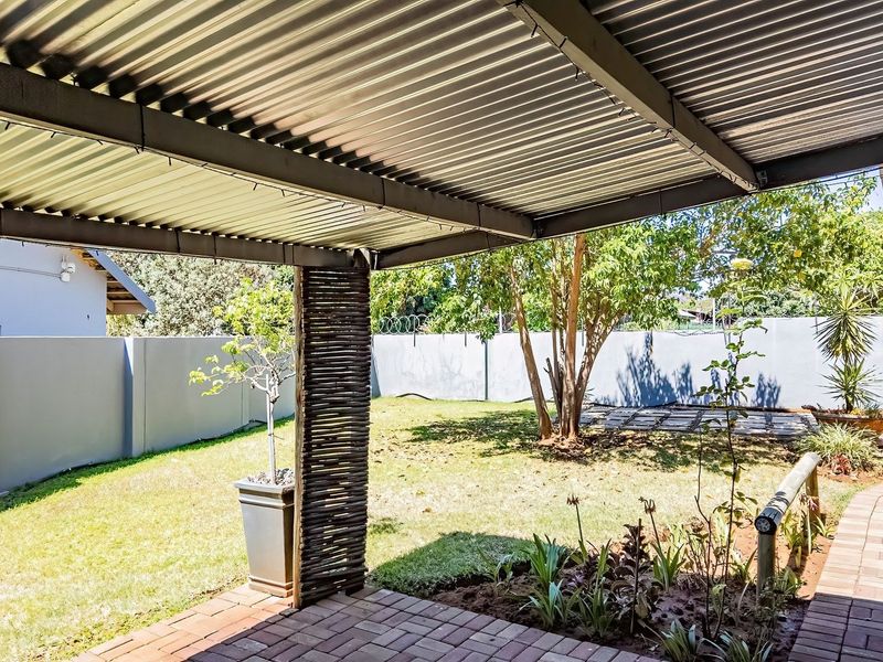 A covered patio area featuring corrugated metal roofing and brick paving, overlooking a private garden with perimeter walling.