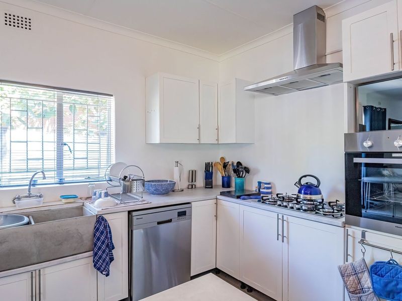 A functional kitchen featuring white cabinetry, stainless steel appliances including a gas hob, extractor fan, built-in oven, and a large sink under a window.