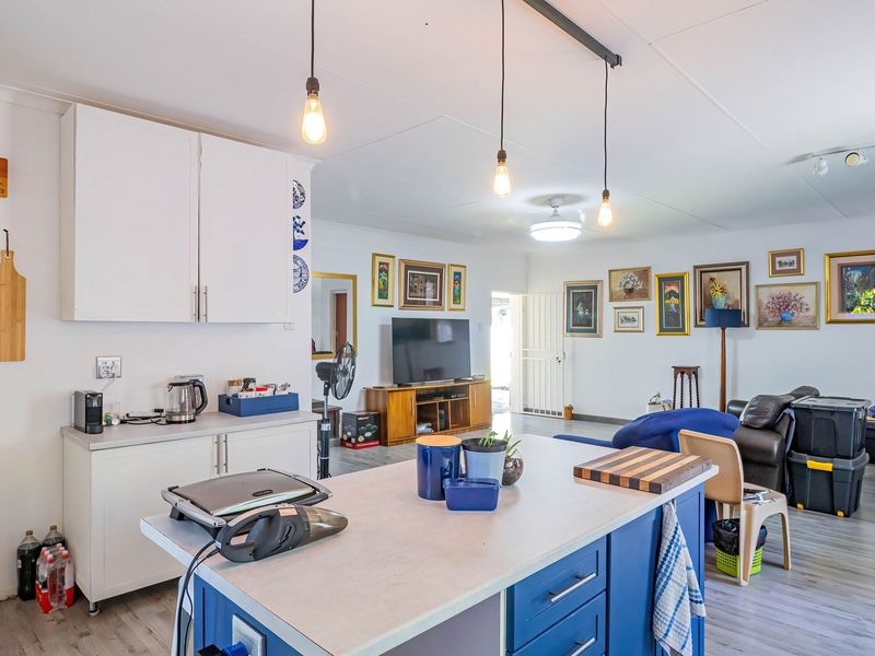 Open-plan living area featuring a central kitchen island with blue cabinetry, pendant lighting, and light-toned laminate flooring throughout the combined space.