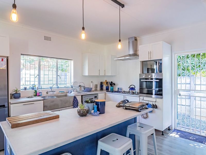 Modern kitchen featuring a central island, built-in oven and microwave, stainless steel sink, and white shaker-style cabinetry with direct access to the exterior.