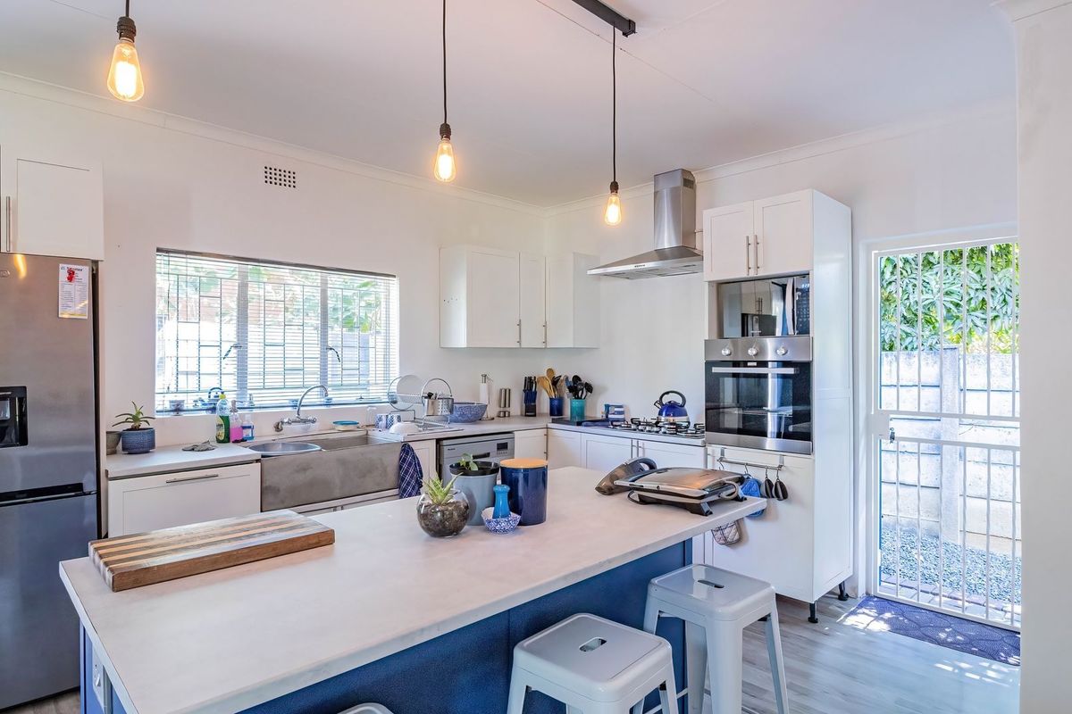 Modern kitchen featuring a central island, built-in oven and microwave, stainless steel sink, and white shaker-style cabinetry with direct access to the exterior.