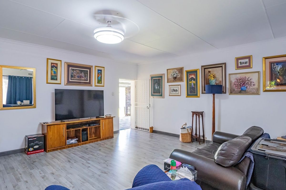 A spacious living room featuring light-toned laminate flooring, a ceiling fan, and direct access to an outdoor area through a security gate.