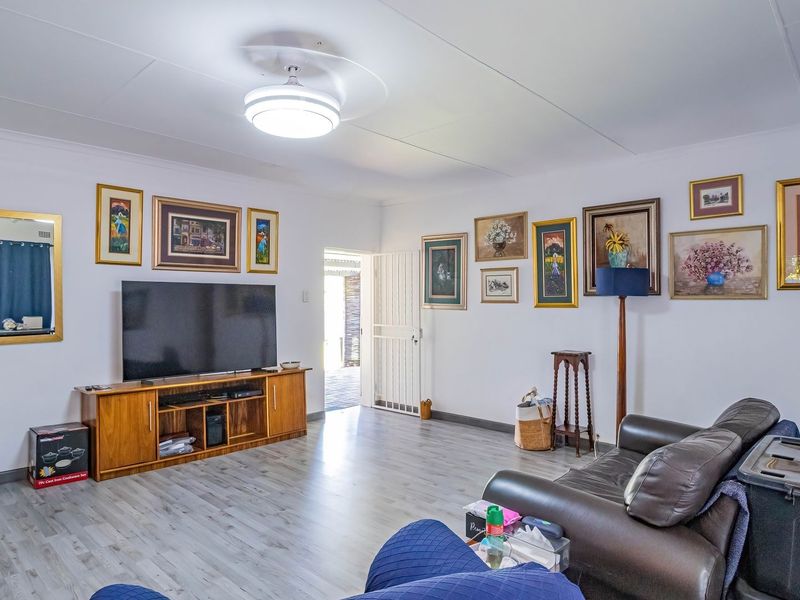 A spacious living room featuring light-toned laminate flooring, a ceiling fan, and direct access to an outdoor area through a security gate.