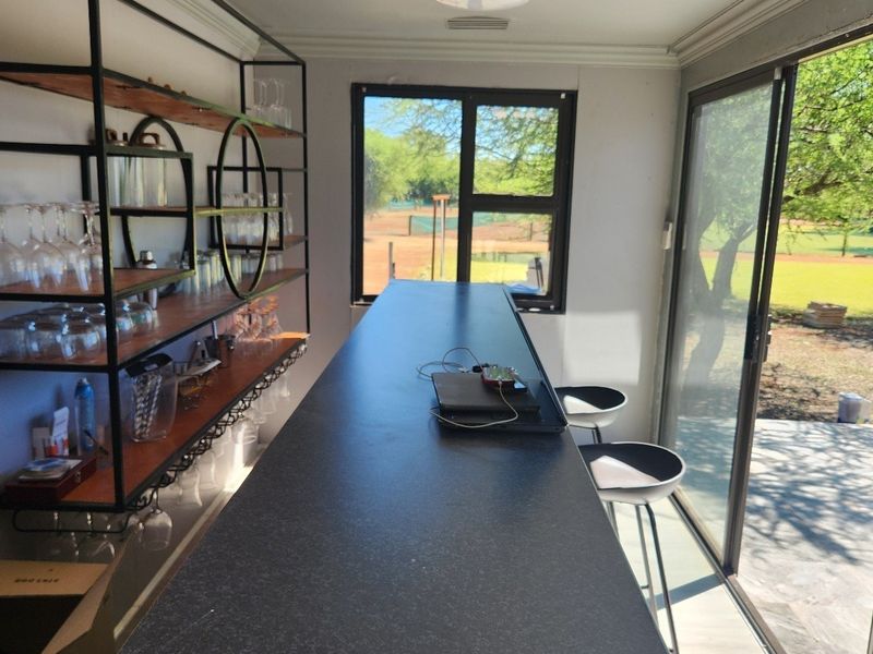 A well-appointed bar area featuring a sleek built-in counter, industrial-style wall shelving, and large sliding glass doors opening to the garden.