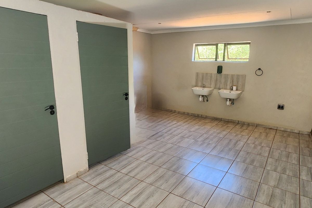 A spacious, empty bathroom featuring dual wall-mounted washbasins, tiled flooring, and two solid doors, offering a functional layout ready for final finishes.