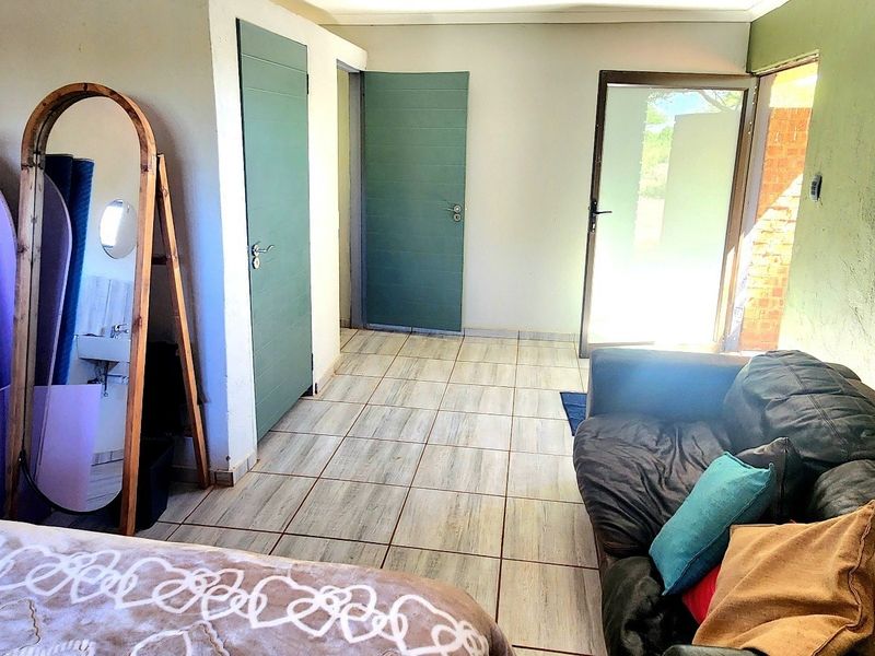 A bedroom featuring tiled flooring, multiple internal doors, and a glass door providing access to the exterior, with a small wall-mounted basin area.