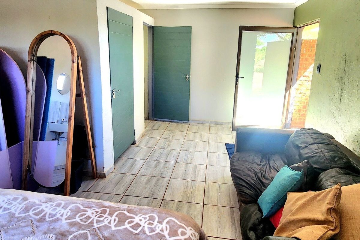 A bedroom featuring tiled flooring, multiple internal doors, and a glass door providing access to the exterior, with a small wall-mounted basin area.