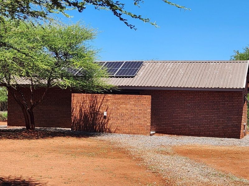 A single-story face brick farm building featuring a corrugated metal roof and installed solar panels, set within a natural landscape.
