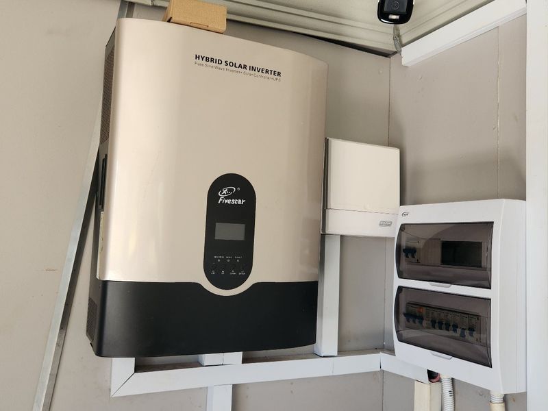 A wall-mounted hybrid solar inverter system paired with an electrical distribution board, providing efficient power management infrastructure.