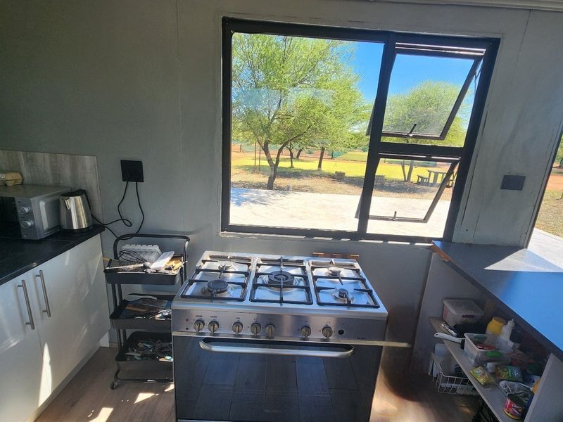 A functional kitchen area featuring a gas stove, laminate countertops, and large windows overlooking the farm grounds.