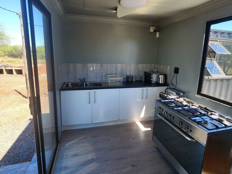 A compact kitchen featuring white cabinetry, a stainless steel gas stove, and laminate flooring, with direct access to the outdoor area via sliding doors.