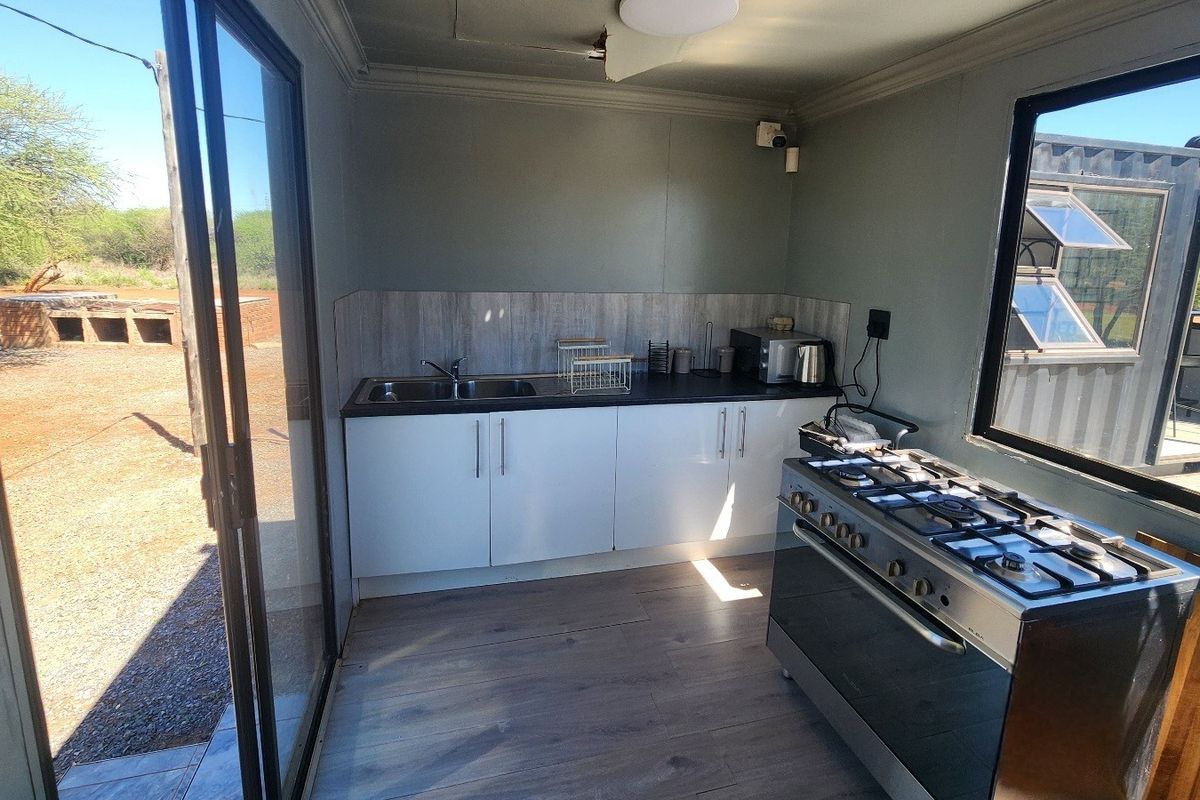 A compact kitchen featuring white cabinetry, a stainless steel gas stove, and laminate flooring, with direct access to the outdoor area via sliding doors.