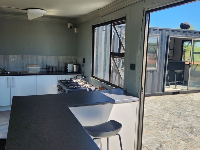 Open-plan kitchen area featuring built-in cabinetry, gas hob, and direct access to a tiled outdoor patio through sliding glass doors.