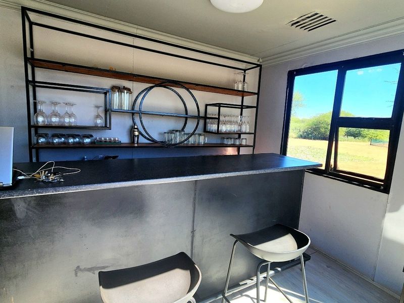 A dedicated bar area featuring a modern built-in counter, industrial-style metal shelving, and a large window providing natural light and scenic views.