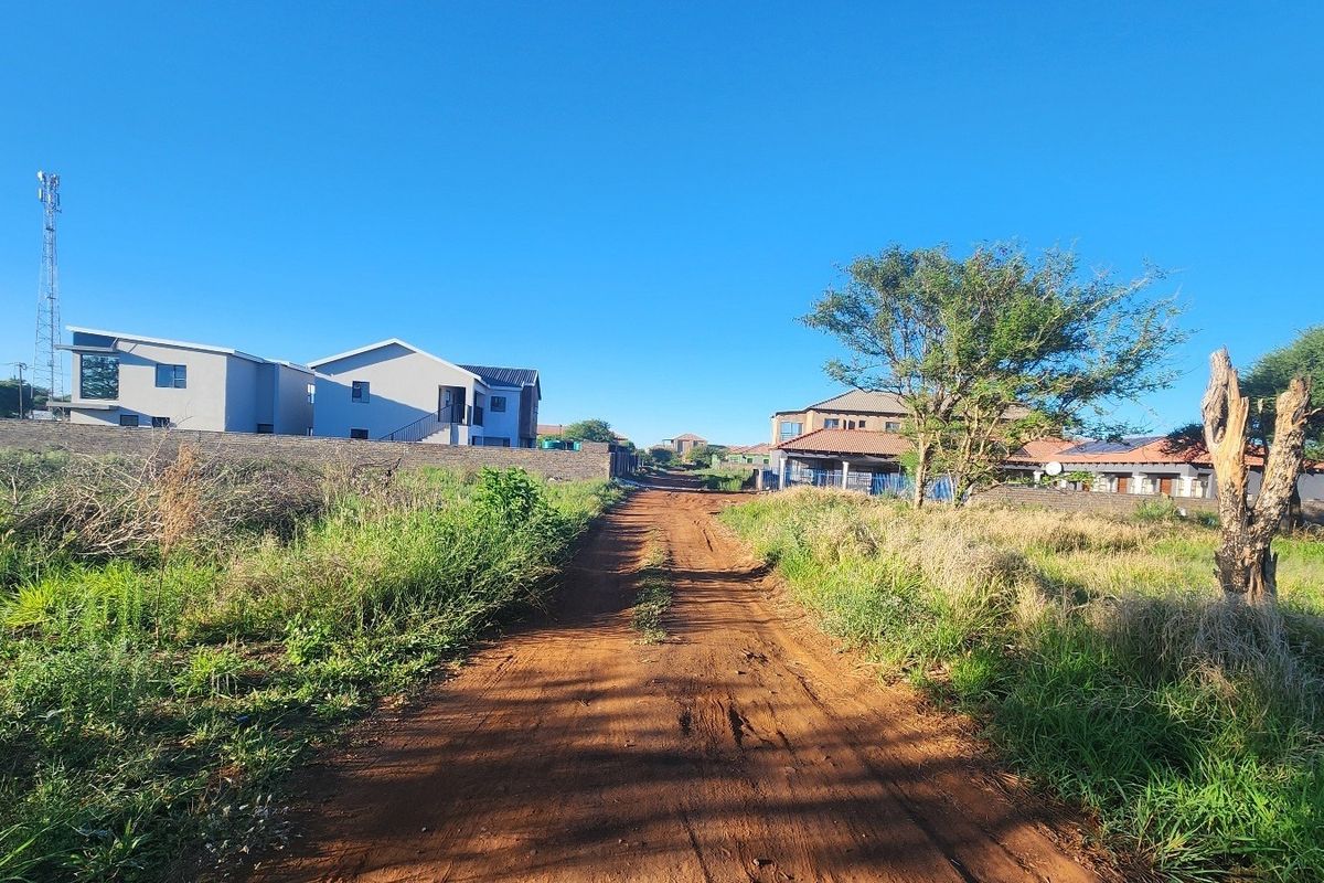 A view of an unpaved access road leading through a residential area with established neighboring properties.