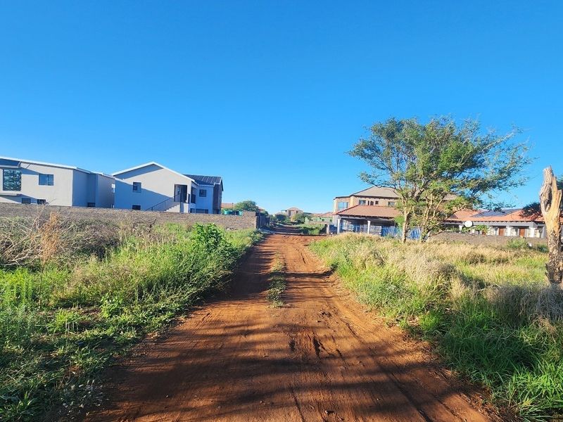 A view of an unpaved access road leading through a residential area with established neighboring properties.