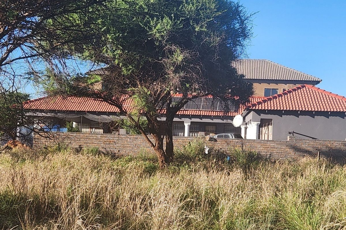 View of a residential property featuring a tiled roof, solar panels, and a brick boundary wall, viewed from an adjacent vacant plot.