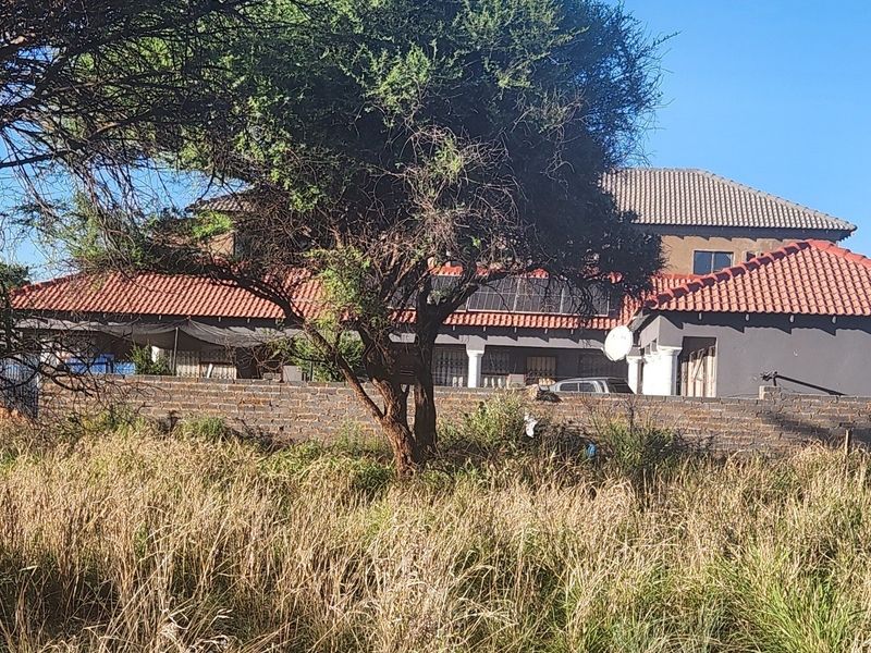 View of a residential property featuring a tiled roof, solar panels, and a brick boundary wall, viewed from an adjacent vacant plot.
