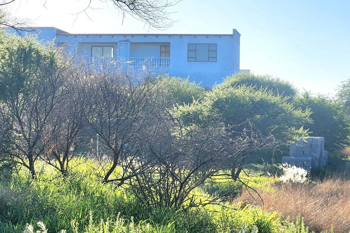 Rear view of a residential property featuring a balcony and established surrounding vegetation on a vacant land plot.