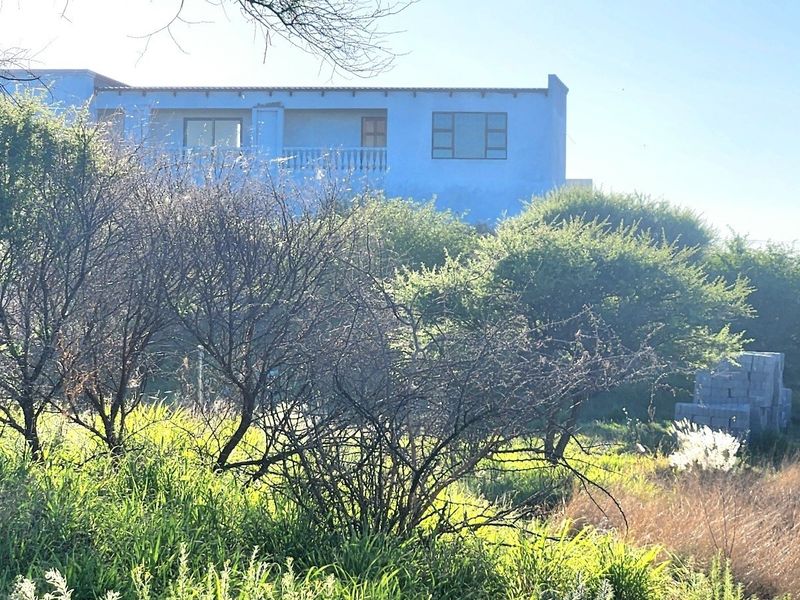 Rear view of a residential property featuring a balcony and established surrounding vegetation on a vacant land plot.