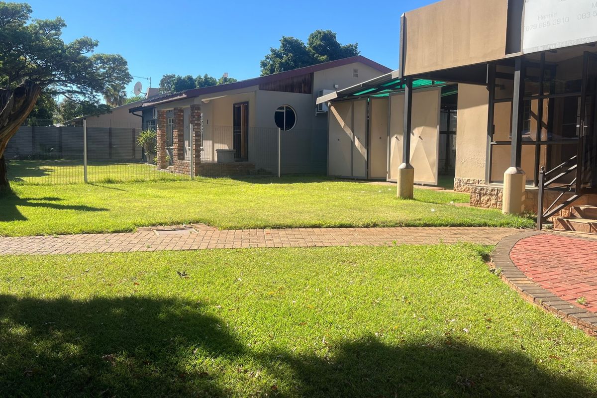A spacious rear garden featuring a well-maintained lawn, paved walkways, and a covered patio area attached to the main dwelling.
