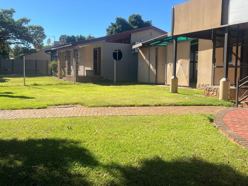 A spacious rear garden featuring a well-maintained lawn, paved walkways, and a covered patio area attached to the main dwelling.