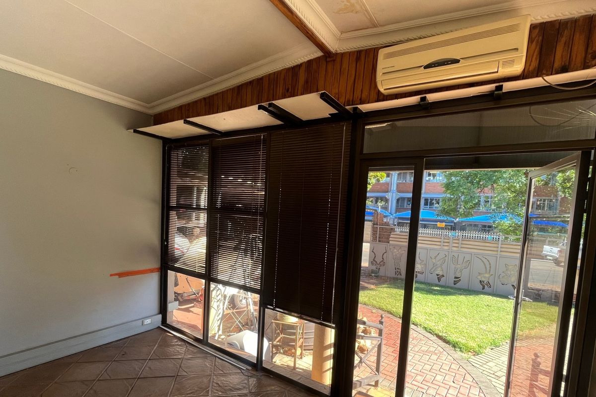An empty living room featuring tiled flooring, a split-system air conditioner, and large aluminium sliding doors providing access to the outdoor area.