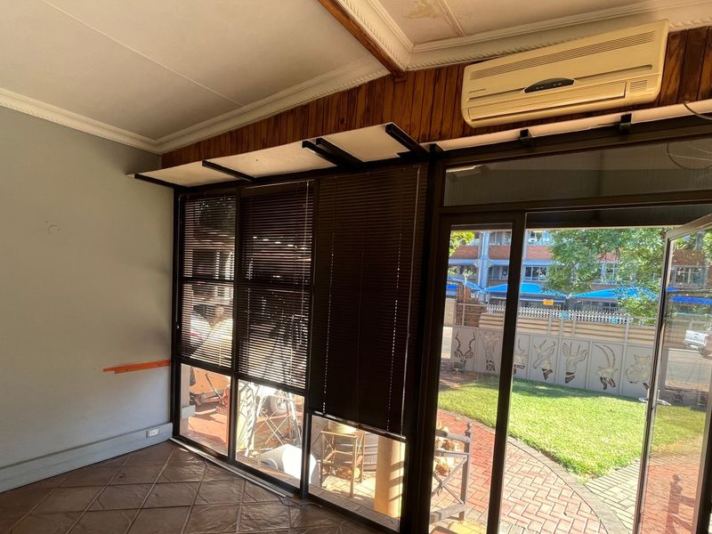 An empty living room featuring tiled flooring, a split-system air conditioner, and large aluminium sliding doors providing access to the outdoor area.