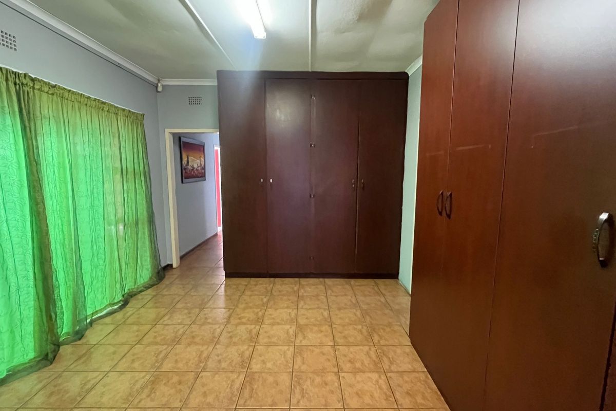 A spacious bedroom featuring extensive built-in cupboards, tiled flooring, and direct access to an adjacent hallway.