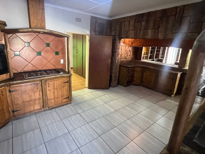 A rustic-style kitchen featuring wooden cabinetry, a built-in oven and hob, and a distinctive stone-cladding feature wall with tiled flooring.