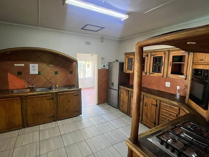 A spacious kitchen featuring rustic wooden cabinetry, a built-in oven, gas hob, and tiled flooring, offering a functional layout with potential for modern updates.