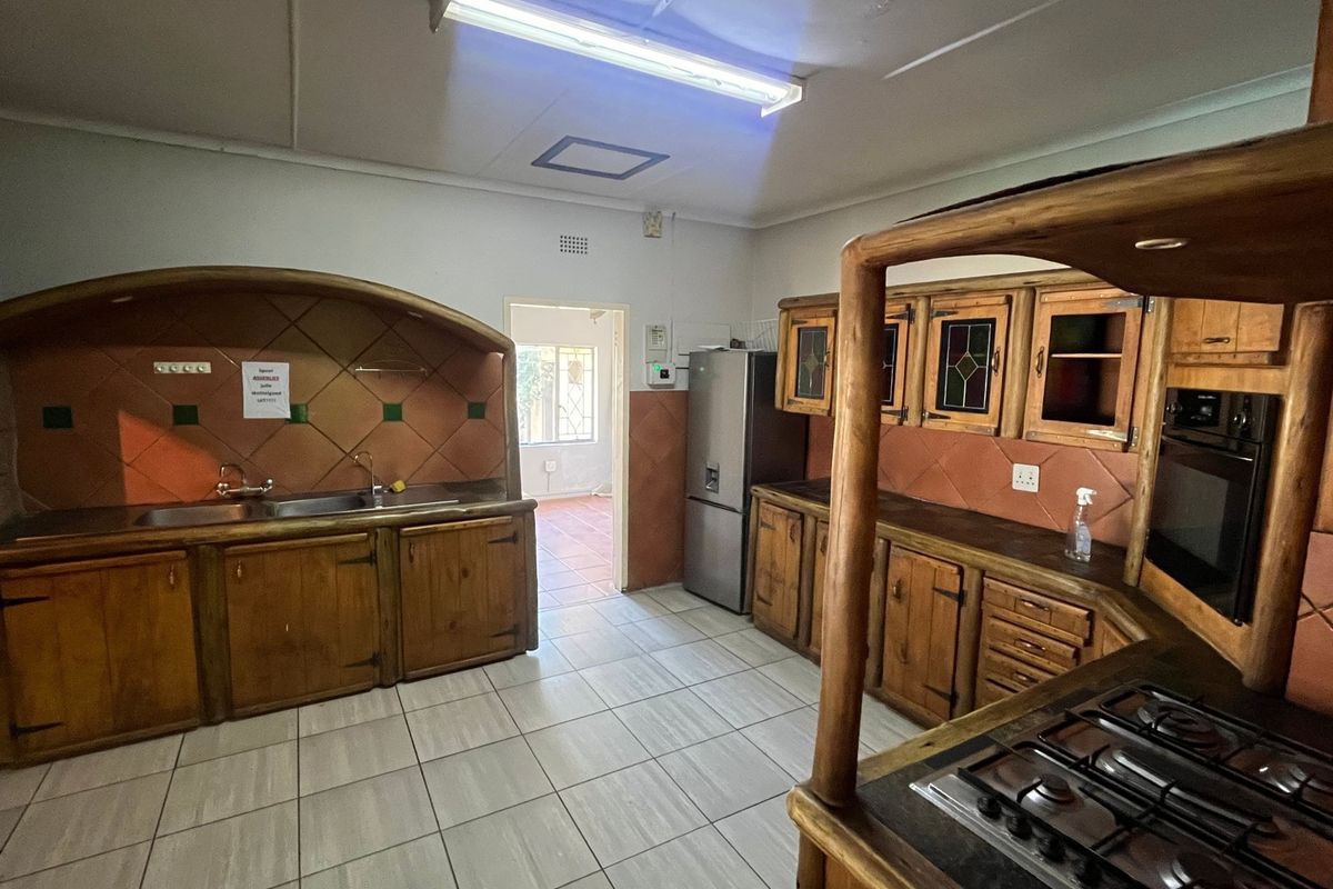 A spacious kitchen featuring rustic wooden cabinetry, a built-in oven, gas hob, and tiled flooring, offering a functional layout with potential for modern updates.