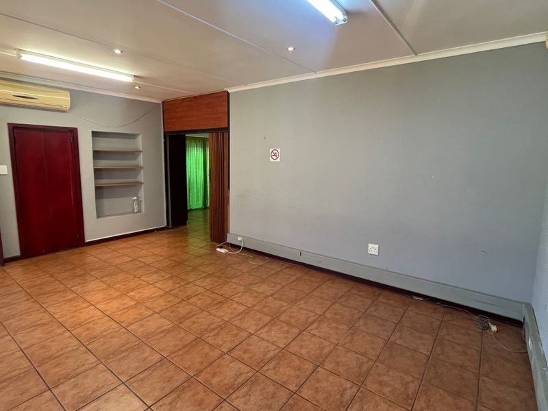 An empty living area featuring tiled flooring, built-in shelving, and an air conditioning unit, offering a blank canvas for potential renovation.